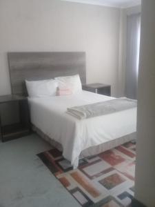 um quarto com uma cama grande com lençóis brancos e almofadas em JBC Guest House em Bushbuckridge