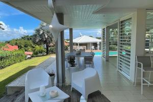une terrasse avec des chaises blanches, une table et une maison dans l'établissement Villa Bahia, luxueuse maison d'architecte., à Petit-Bourg