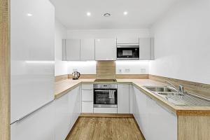Beautiful Apartment in Surrey Quays في لندن: مطبخ أبيض مع دواليب بيضاء ومغسلة
