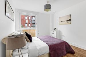 Beautiful Apartment in Surrey Quays في لندن: غرفة نوم بيضاء بسرير وكرسي
