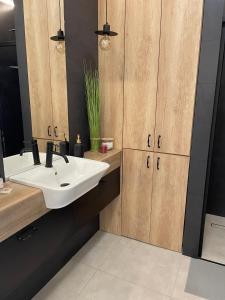 La salle de bains est pourvue d'un lavabo blanc et de placards en bois. dans l'établissement Stylowy Apartament przy Manufakturze w samym centrum Łodzi, à Łódź