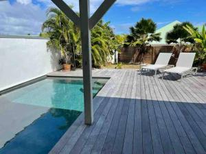 a swimming pool with a wooden deck and chairs next to a house at Orient Bay villa in Saint Martin