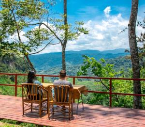 a man and woman sitting at a table on a deck with a view at Cabañas Don Tito in Pejibaye