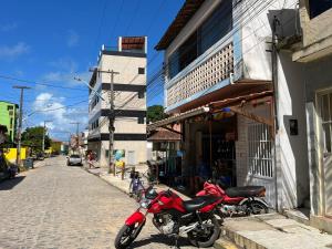 uma moto vermelha estacionada ao lado de um edifício numa rua em Apartamento Simples e completo em Maragogi