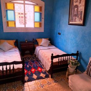 twee bedden in een kamer met blauwe muren en een raam bij Riad Ennaciri in Safi