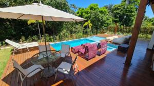 eine Holzterrasse mit einem Tisch, Stühlen und einem Sonnenschirm in der Unterkunft Casa Ofir - Simplesmente um Paraíso in Praia do Forte