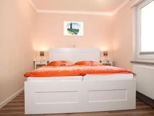 - une chambre avec un grand lit blanc et des draps orange dans l'établissement Meertied, à Oertzenhof
