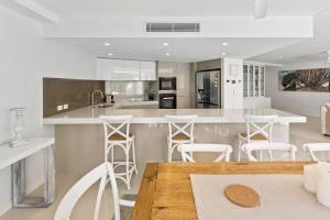 a kitchen with a wooden table and white stools at The Garland at Rainbow Bay in Gold Coast