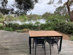 een houten tafel en twee stoelen op een terras met een rivier bij Tranquil Garden Studio with Stunning Lake Views in Ocean Grove