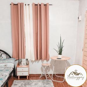 1 dormitorio con cortinas rosas, mesa y cama en Malunggay Apartments en Mariveles