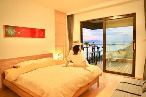 a woman sitting on a bed in a bedroom with a balcony at Colorful Yunnan Absolutely Beautiful Dian B&B in Kunming