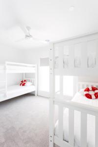 a white bedroom with white bunk beds with red pillows at Rosebay - Coastal Holiday Home in Rosebud