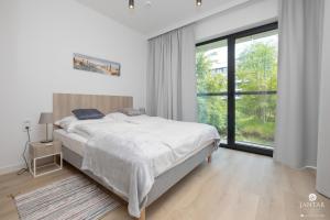 a white bedroom with a bed and a large window at Shellter Apartments 117 L - by Jantar Apartamenty in Rogowo