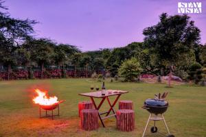a grill and a table with a fire in a field at StayVista at Idyllic Farmhouse - A Glasshouse with Outdoor Pool in Gurgaon