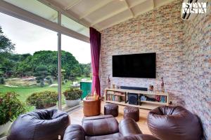 a living room with leather furniture and a tv on a brick wall at StayVista at Idyllic Farmhouse - A Glasshouse with Outdoor Pool in Gurgaon