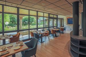 um restaurante com mesas e cadeiras e janelas grandes em L'HÔTEL DES BAINS - Salles-la-Source em Salles-la-Source