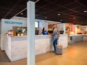 una persona in piedi presso il bancone della reception in un ufficio di ibis budget Amsterdam Airport a Badhoevedorp