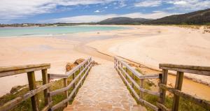 einen Sandstrand mit einem Holzzaun und dem Meer in der Unterkunft CASA AREALBA Casa con piscina muy cerca de las playas de San Xurxo y Doniños in Ferrol