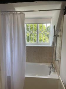 La salle de bains est pourvue d'un rideau de douche blanc et d'une fenêtre. dans l'établissement Holly Cottage, 2, Northbrook Park, Farnham-up to 6 adults, à Farnham 19 autres photos