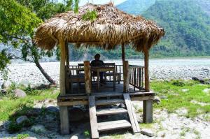 a person sitting at a table under a straw hut at Beyond Brahmaputra & Eagles Nest 