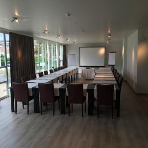 einen Konferenzraum mit einem langen Tisch und Stühlen sowie einem Bildschirm in der Unterkunft Hotel Les Dunes in De Haan