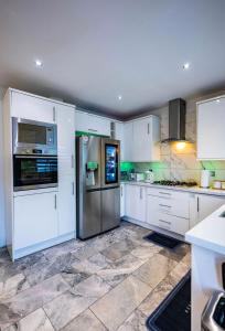 eine Küche mit weißen Schränken und einem Kühlschrank aus Edelstahl in der Unterkunft UPPAMOST LUXURY HOME LONDOn in Dagenham