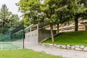 kort tenisowy przed budynkiem z drzewem w obiekcie Vital Hotel Flora w mieście Comano Terme