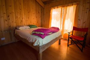 Cama en habitación de madera con silla roja en El Refugio Casa de Montaña en San Martín de los Andes