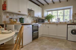 cocina con armarios blancos, mesa y ventana en The Old Potting Shed, en Kirkbymoorside