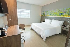 a hotel room with a white bed and a desk at GHL Style Yopal in Yopal