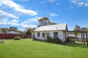 una pequeña casa blanca con un patio verde en Katisha Cottage, en Paynesville 5 fotos más