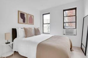 um quarto branco com uma cama grande e 2 janelas em Warm 3 BR Loft in Midtown em Nova York