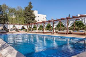 una piscina con sombrillas y sillas blancas en Zafiro Palmanova, en Palmanova