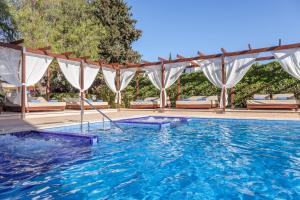 een zwembad met blauw water en witte gordijnen bij Zafiro Palmanova in Palmanova