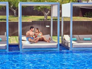 un hombre y una mujer sentados en las camas junto a una piscina en Zafiro Palace Palmanova en Palmanova