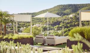 a patio with a white couch and chairs and an umbrella at Zafiro Palace Andratx in Camp de Mar