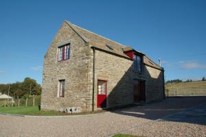 an old stone building with a red door on a road at Craiglea Barn in Latheron