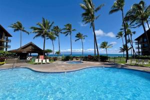 een groot zwembad met palmbomen en de oceaan bij Papakea Resort G406 in Lahaina