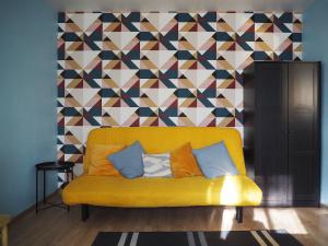 un sofá amarillo en una habitación con una pared geométrica en Cozy city center apartment, en Visaginas