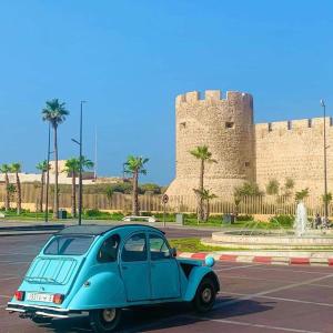 een blauwe auto geparkeerd op een parkeerplaats voor een kasteel bij Riad Ennaciri in Safi