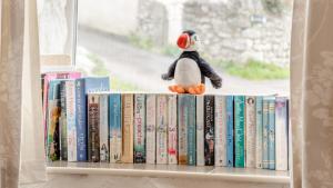 a shelf with a stuffed penguin sitting on top of books at Frog Cottage in Llanmadoc