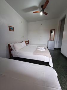 a bedroom with a white bed with a ceiling fan at Pousada da Jaqueira - EPP in Rio das Ostras