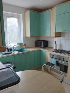 a kitchen with green cabinets and a table and a window at 2 Bed Mill Hill Flat in Mill Hill