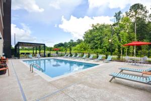 einen Pool mit Stühlen und Sonnenschirmen in einem Hotel in der Unterkunft Home2 Suites By Hilton Opelika Auburn in Opelika