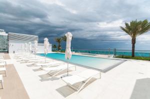a pool with chairs and umbrellas and the ocean at Monte Carlo Suites in Miami Beach in Miami Beach