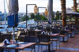 una fila de mesas y sillas en un restaurante con barcos en For Harbor Travelers, en Pireo