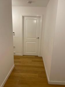 een lege hal met een witte deur en houten vloeren bij Amazing Luxury Double Bedroom with en-suite shower and free parking with a Sound bar & smart TV in a two bed Apartment I live in the 2nd room in Belvedere