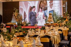 a group of tables in a banquet hall with a large screen at Hotel Majestic Saigon in Ho Chi Minh City