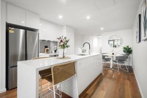 a white kitchen with a sink and a counter with chairs at Founders Lane Apartments by Urban Rest in Canberra