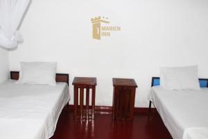 two beds with white sheets and wooden tables in a room at Marien Inn in Galle
